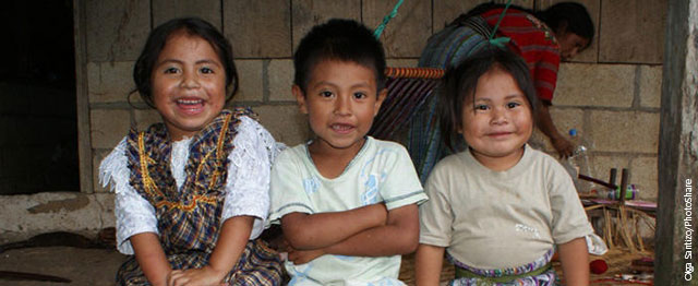 Three smiling children in Guatemala sit in a row.
