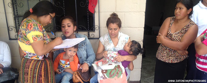 women with children wait in line at a clinic while a nurse checks them in