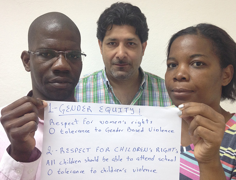 Three people holding card that says "1 Gender Equity, respect for women's right, no tolerance to gender based violence. 2 Respect for children's rights, all children should be able to attend school, no tolerance to children's violence"