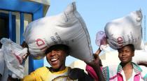 Two women carry bags of supplies on their heads.