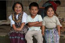 Three smiling children sit in a row in Guatemala.